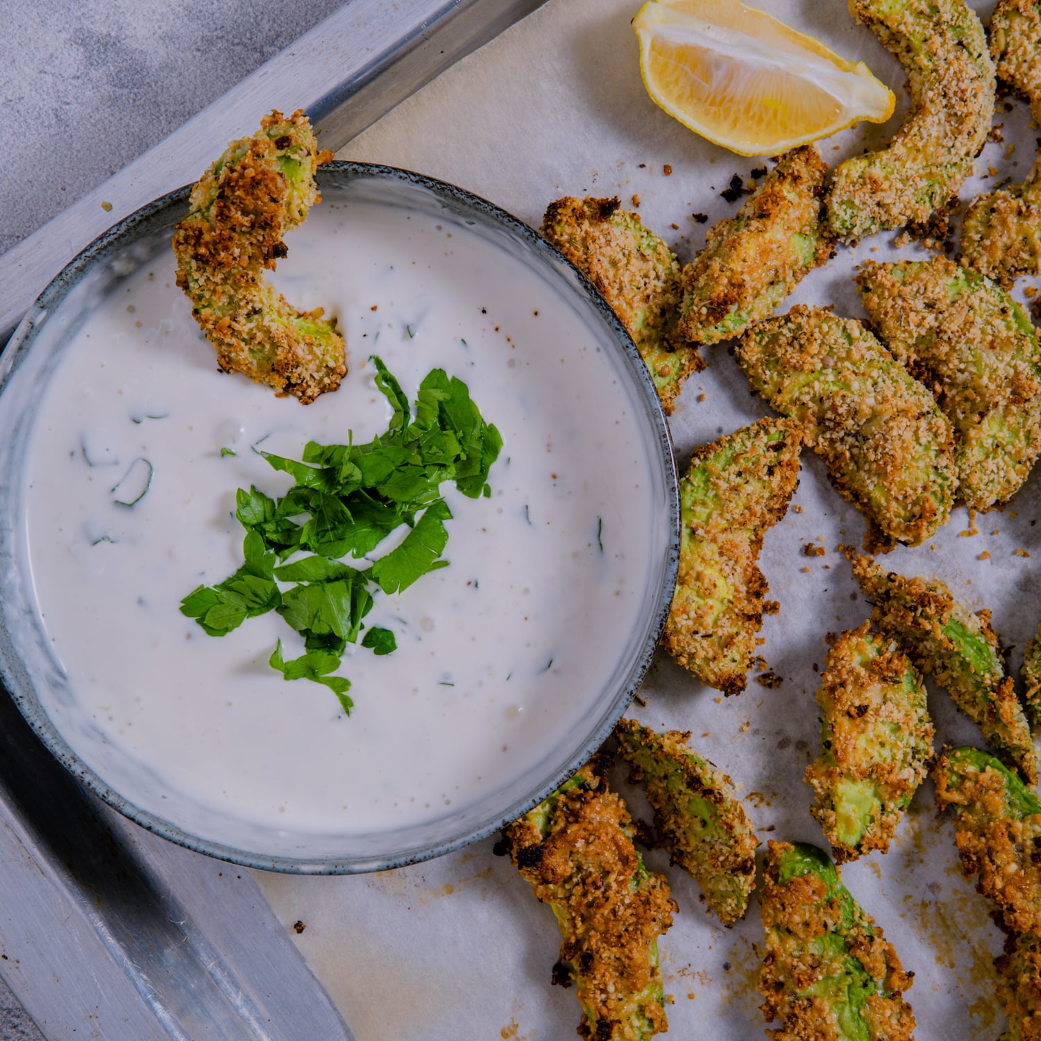 Garlic parmesan baked avocado fries served with creamy lemon dipping sauce and fresh parsley garnish
